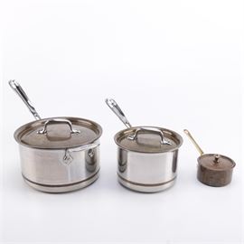 Steel Cooking Pots Featuring All-Clad: A group of cooking pots. There are three of various sizes with two All-Clad “copper core” lidded pots. The smallest pot features a brass finial and handle and is unmarked.