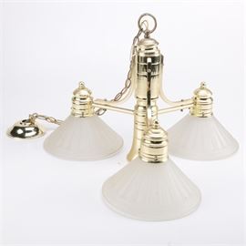 Gold Toned and White Glass Chandelier: An Art Deco gold tone and white glass chandelier. The light is metal with a gold tone finish and features a dome style mount and chain. Other features include a pillar shaped center piece with a socket and three curved and straight arms with metal holders that display a fluted and frosted glass lamp shade with a paneled design.