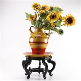 Terre è Provence Hand-Painted Pitcher Vase and Stand: A Terre è Provence hand-painted pottery pitcher vase on stand. The piece is painted in colors of gold and red featuring a band of same color flowers. It includes silk sunflowers and a detached under plate. The pieces sit on a wooden display stand with a black finish. The pottery pieces are marked to the underside.