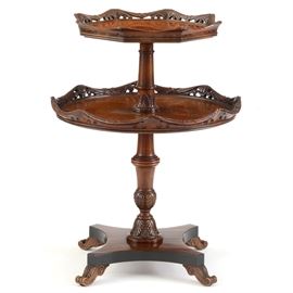 Georgian Style Two-Tiered Dumbwaiter: A Georgian style two-tiered dumbwaiter with a burlwood veneer. This piece has a carved, pierced swag border and a baluster turned pedestal with carved leaves. It rests on scrolled feet.