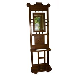 Vintage Hall Stand: A vintage hall stand. This item features a beveled glass mirror, four patinated brass hat hooks, and an umbrella well. It is adorned with both carved and applied details.