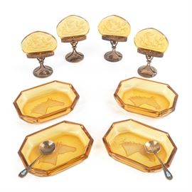 Amber Glass Salt Cellars and Place Card Holders: A grouping of amber glass salt cellars and place card holders. Featured are four octagonal salt cellars with an etched horse’s head to the bottom complete with two miniature silver spoons with a turquoise color design set in the handle. The Russian spoons are marked with a hammer and sickle in a star design and “875”. Also included are four place holders with a Roman etched design into the amber glass and set in antique brass stands.