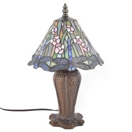 Quoizel Stained Glass Accent Lamp: A small stained glass accent lamp by Quoizel Collectibles. This small decorative lamp features a dragonfly motif in a palette of cool blues and greens with soft pink accents. The finial, pierced cap, stem, and base are made of cast metal with a dark patina. It accepts a single bulb that operates by an on-line switch. It bears the maker’s mark to the inner shade.