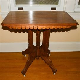 Antique Walnut Side Table: An antique walnut side table. This rectangular table features beveled corners to the chamfered fillet top. It is accented by a scalloped design to the apron and rises on a turned stem with four shaped legs, splayed feet, and original white porcelain casters. Bas relief carvings accent the shaped legs.