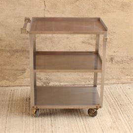 Three Tier Industrial Aluminum Cart on Wheels: An industrial aluminum push cart. This unit has three shelves, the top two of which have rails, and is on rolling casters.