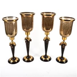 Stemmed Votive Candle Holders: A set of four stemmed votive candle holders. The candle holders have black and brass stems with charm dangles around the tops of the stems. The glass candle cups have opaque gold crackled glass, with brass rims. The set is marked “Made in India”.