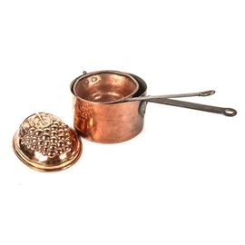 Copper Cookware: A collection of copper cookware. Featured in this collection are a round, handled saucepan, a strainer ladle, and a mold. The mold is oval with a cluster of grapes design and a hook for hanging. No maker’s marks.