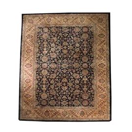 Large Wool Area Rug: A large wool area rug. Featured here is a pure wool, machine made area rug with a black center. This rectangular central section features a floral design in colors of tan, burgundy, sage green and rust. The wide border on the perimeter is gold in color with a different floral pattern. The edge of the rug is black and and there is a tag on the reverse marked “Safavieh, Golden Jaipur Red/Gold 9’ 6” x 13" 6".