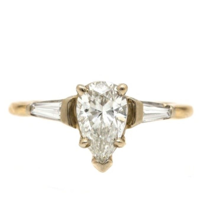 14K Yellow Gold 1.58 CTW Diamond Ring: A 14K yellow gold 1.58 ctw diamond ring. This ring showcases a pear faceted cut 1.28 ct diamond center stone, flanked by two baguette cut diamonds to the shoulders.