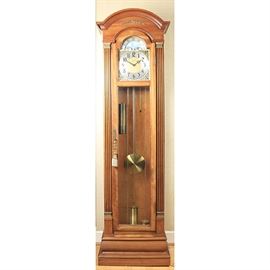 Herschede Grandfather Clock: A Herschede grandfather clock. This free standing clock features a round beveled pediment, reeded side columns and beveled base. Clock has a glass paneled hinged front that opens to the metal face with black numerals ad hands with ship motif second dial on the top. Clock has polished brass weights and pendulum and stands in a medium stained wooden case with glass paneled sides.