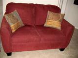 Red upholstered loveseat with two pillows.