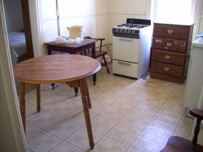 Round wood kitchen table, wood chairs, stove, dresser.