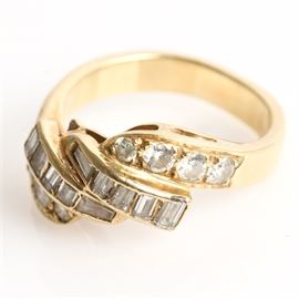 18K Yellow Gold and 1.00 CTW Diamond Bypass Ring: .An 18K yellow gold bypass ring featuring two rows of center invisible set baguette cut diamonds flanked by round cut diamond side stones. The diamonds have a total carat weight of 1.00 ctw.