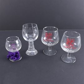 Commemorative Barware Featuring The Glen Burne Class of 1979: A group of clear wine glasses with school stamps. There are four in total with wide bowls that read, “Glen Burne Class of 1979”. There is a glass with a tapered stem with floral and ball accents. Another glass reads, “Plains 25th Silver Anniversary Class of 1950”.