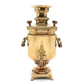 Antique Russian Brass Samovar: A turn of the century Russian brass samovar. The samovar features a barrel-shaped reservoir in polished brass, having turned wood handles and knobs, with an open steam vent to top and decorative brass spigot key. The tin lined samovar rests on a square self footed base and bears markings and medallion stamps from the Russian imperial maker Batesheva, with additional stamped awards and exhibition medals to the front and base. Samovars were first introduced to Russia during the mid-1700s, becoming an important center of cultural life.