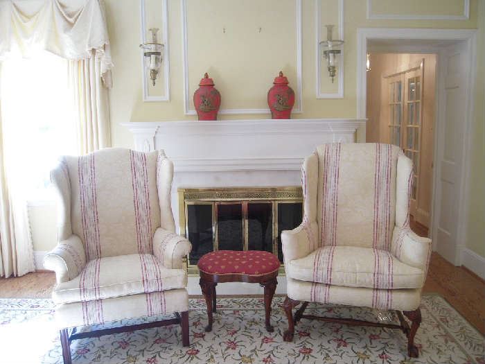 Living Room:  Two ivory/raspberry stripe wingback chairs are almost identical.  The one on the left has Chippendale style legs and rolled arms while the one on the right has claw/ball feet and narrow flat arms. Both were upholstered by LUTTRELL UPHOLSTERING.    Did you know that this style of chair was developed in England in the 1600's where cold weather made the roaring fireplace the gathering spot of the house?  The original style was created to keep women warm as they lounged in the wingback chairs to protect their upper chests from cold drafts. The design gained popularity in the early 1700's and eventually morphed from a wooden chair to one with upholstery.   On the mantel are two red/gold urns with lids; attached to the wall [but easily removable] is a pair of brass/glass candle hurricanes.    