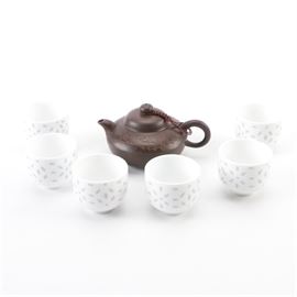 Miniature Asian Tea Set: A miniature Asian tea set. This set includes seven ceramic pieces. The teapot is brown in color with incised designs, images of a mouse, and character letters to the surface. A lid is attached to the handle by a red braided cord. The cups are white with gray starburst patterns. All pieces are marked to the bottoms.