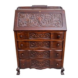 Nineteenth-Century Oak Secretary: A nineteenth-century oak secretary. The secretary features a molding rail along the back and sides of the top. The front features a slant-front hinged panel with carved flourishes, and it opens to reveal a work space with divided compartments and a small drawer. Below are four dovetailed drawers, which have scalloped, convex fronts embellished with carved flourishes in the center panels. They are fitted with pairs of round wood knobs and brass keyholes. The chest has straight sides, and it rests on carved ball and claw feet. No maker’s marks.