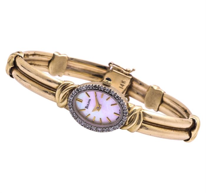 Bulova 14K Yellow Gold, Mother of Pearl, and Diamond Wristwatch: A Bulova 14K yellow gold, mother of pearl, and diamond wristwatch. This item features a oval watch case with the rim set in single cut diamonds. The mother of pearl dial has gold tone hands and hour markers. The 14K yellow gold bracelet fastens with a decorative box tab which has a safety chain.