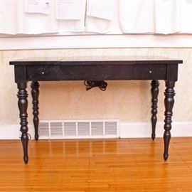 Vanity Desk with a Flip-Up Top: A vanity desk with a flip-up top. Features a flip-up center section that opens to reveal a sunken interior space with an interior mirror and electrical outlet access, flanked by two small drawers with button pulls that open to the front. The table rises on four turned and tapered legs.