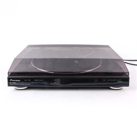 Pioneer Automatic Turntable: A Pioneer turntable, model PL-990. This full automatic stereo turntable presents in black, featuring a speed adjust knob and various push buttons. Comes with a hinged dust cover and power/connectivity cords.