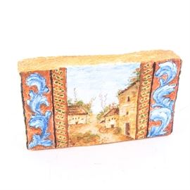 Italian Style Painting on Paper Mache Brick: An Italian style painting on a paper mache brick. This painting depicts a peaceful villa scene at the center flanked by a decorative crosshatch border and blue scroll patterns to either end. This piece is unmarked.