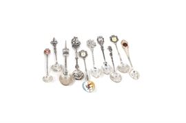 800 Silver Collector Spoons: A collection of 800 silver collector spoons. This collection is complete with eleven spoons. The spoons are in a variety of styles depicting various places and maker’s marks on the back.