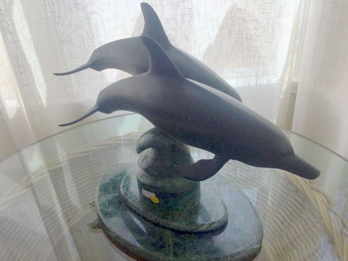 Skimming bronze dolphins sculpture with a green marble base.