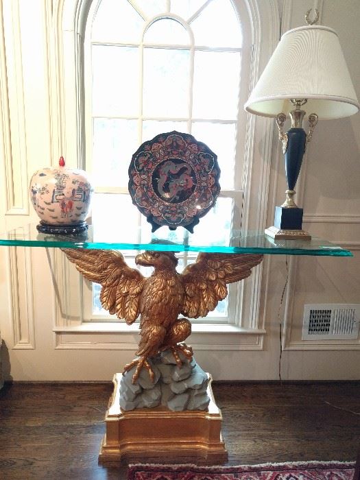Close-up of one of the vintage Italian gilt wood eagle console tables; very thick ogee beveled glass tops. Large Asian cloisonne plate, on stand, one of a pair of black/gold metal lamps.