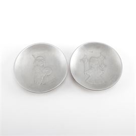 DeGrazia Pewter Plates: A pair of Degrazia pewter plates. This pair of pewter plates features a limited edition plate titled, Pima Drummer Boy depicting a raised image of a young tribal boy with drum and traditional clothes and is numbered 0671/3000 and a plate titled, Heavenly Blessings , a limited edition plate numbered 0678/3000 and depicts a raised image of a young tribal girl with dream catchers. Both plates are marked to the undersides.