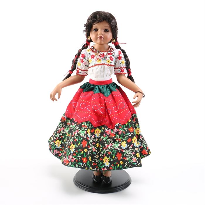 The Danbury Mint "Rosaline" Doll: A Rosaline doll by The Danbury Mint. This doll features brown hair and brown eyes with a porcelain body. The doll has fabric clothing including a white blouse with an ankle-length skirt in floral patterns and metal jewelry with beaded accents. The doll has a maker’s mark from The Danbury Mint and comes with a Certificate of Authenticity that reads “Rosaline The Cry for Independence Doll” referencing Mexican Independence Day. A wooden display stand is also included.