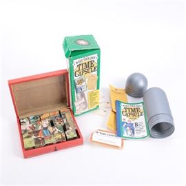 Block Puzzle Set and Time Capsule Toy: A block puzzle set and a time capsule toy. This lot offers a “Make Your Own Time Capsule” kit which includes a grey plastic pill shaped capsule, an illustrated idea book and log, identification tags, and more. The kit comes with the original packaging. Also included is a block puzzle set in a wooden case, with printed images on various sides of the blocks which form different pictures.