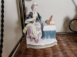one of the five senses figurines depicting the sense of sight. Woman is at a dressing table looking at herself in a mirror a cape is around her shoulders and a small cap is on her head and she is holding a flower in her hand. meissen crossed blue swords plus incised numbers E3 and 152 under glaze on reverse side