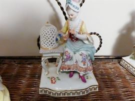 figurine depicting the "Sense of Hearing" woman seated at a birdcage which has an open door, she appears to be feeding or petting the bird inside she is wearing a turban style head covering.Meissen crossed swords mark plus incised numbersE4 and137 under glaze on reverse side. 