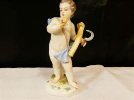 Meissen figurine depicting a cherub holding a sheaf of wheat on his arm and a curved blade knife in his hand has blue drape around shoulders and lower torso german late 19th century hard-paste porcelain polychrome detail