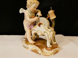 Meissen figurine of a cherub standing at a grinding wheel sharpening his arrows he is wearing a pink drape around his lower torso german late 19th century hard-paste porcelain polychrome detail  4 1/2 inches high.