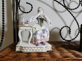 figurine depicting the "sense of taste" woman sitting at a table having dinner with a plate of fruit and a bottle of wine sitting before her. excellent condition