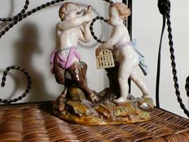 Meissen figurine depicting a baby satyr with the head and torso of a cherub and the legs of a goat  he is holding a bird in his hands and a female cherub stands beside him holding a birdcage. Meissen blue crossed swords mark plus the incised numbers 82 and 147 under glaze on reverse side.