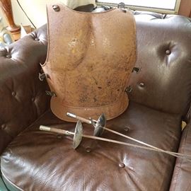 Rusty metal breast plate and fencing swords displayed on brown vinyl sofa.  (Real?  Hollywood?)