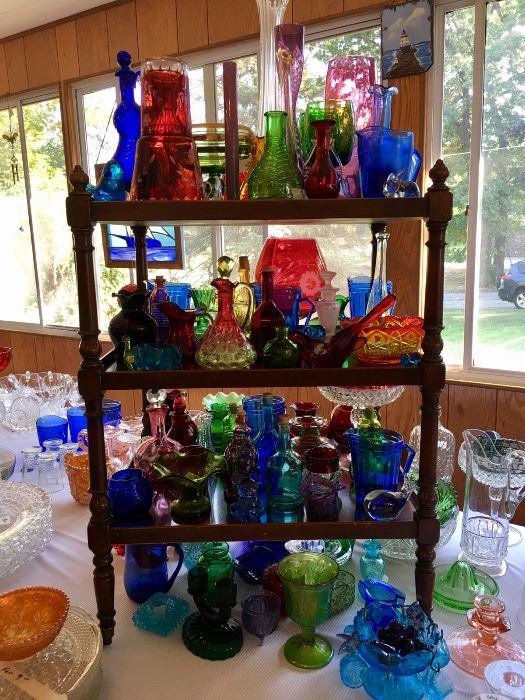 Display of a variety of vintage and antique, uniquely shaped glass bottles, cruets, and other glassware in all the colors of the rainbow!