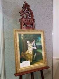 Second of two large carved mahogany easels holding an oil painting of figures dancing 