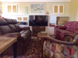 Great Room features electric dual-reclining sofa, 55" Samsung Smart TV, burgundy leather sofa, multi-color armchair with wood arms, Kathy Ireland large area rug.