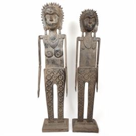 Burmese Carved Wood Ancestor Figures: A pair of Burmese hand-carved wood “ancestor” figures. The tall wood sculptures are flat in profile, with carving on the fronts, and plain on the backs. Both figures are depicted with grinning faces and spiked hair, long earrings, and collar-style necklaces, wearing pants that have carved ring patterns. They have hinged wooden arms, which bend at the elbows. The legs are straight and square, and are without feet. They attached to square wood bases, and are not marked.