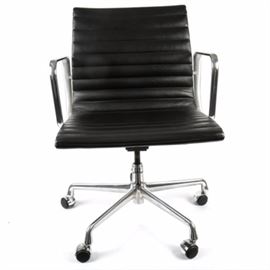 Eames Reproduction "Aluminum Group Management Chair": A copy of a vintage Eames “Aluminum Group Management Chair”. The chair features black faux leather upholstery and a chrome metal frame. The adjustable swivel chair features a square back and a continuous seat, padded and upholstered in black faux leather with horizontal stitching, creating puffed ribs. The high arms are made of chromed metal, and there are adjustment knobs to the underside, which are made of chrome metal. The chair rests on a column attached to a cast chrome metal base, with five legs that are fitted with casters. There is a label on the back of the frame marked “EA335 – VD L – 258 – 3060049 – 09072005”.
