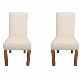 Contemporary Upholstered Side Chairs with Slipcovers: A pair of matching, contemporary upholstered side chairs, with slipcovers. The chairs have clean lines, featuring chair backs with straight angles. The backs and seats are padded and upholstered in a white woven fabric, and the chairs rest on straight, square wood legs, stained in a medium color. The chairs come with off-white, lightweight woven fabric slipcovers. No maker’s marks.