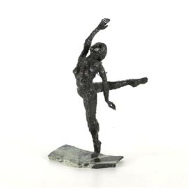 Signed Iron Sculpture of a ballet Dancer on Marble: An iron sculpture of a dancer on marble. This expressive piece presents the figure of a dancer standing on one leg with the other leg elevated, hand lifted above her head. The textured surface of the figure is finished in a dark patina, and the piece stands on a thin marble base with striations. This piece is signed “Olson”.