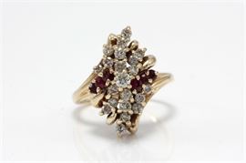 14K Yellow Gold Diamond and Ruby Ring: A yellow gold bypass shank with round cut diamond prong set to the center surrounded by a spray of round cut diamonds and rubies in a marquise shape to the top.