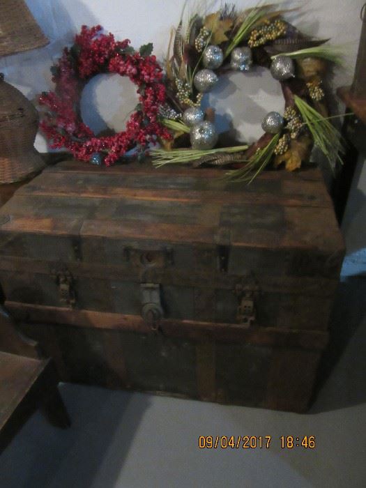 Two Christmas wreaths sit on a flat top trunk  