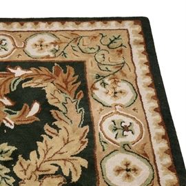 Machine Made Area Rug: A machine made area rug. The rug features a black ground that is decorated with a scrolling acanthus leaf motif in hues of tan, sage and cream. The rug features a coordinating border.
