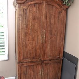 Walnut Armoire by Ethan Allen: An armoire by Ethan Allen. This piece is constructed from walnut, and it features domed double doors which open to three removable shelves and a slide-out, turning base to accommodate a television. The lower section has double cabinet doors with recessed panels which open to a height-adjustable shelf with slide-out platform over a locking machine dovetailed drawer with divided storage compartments. The armoire also has brass hardware and rests on bun feet.